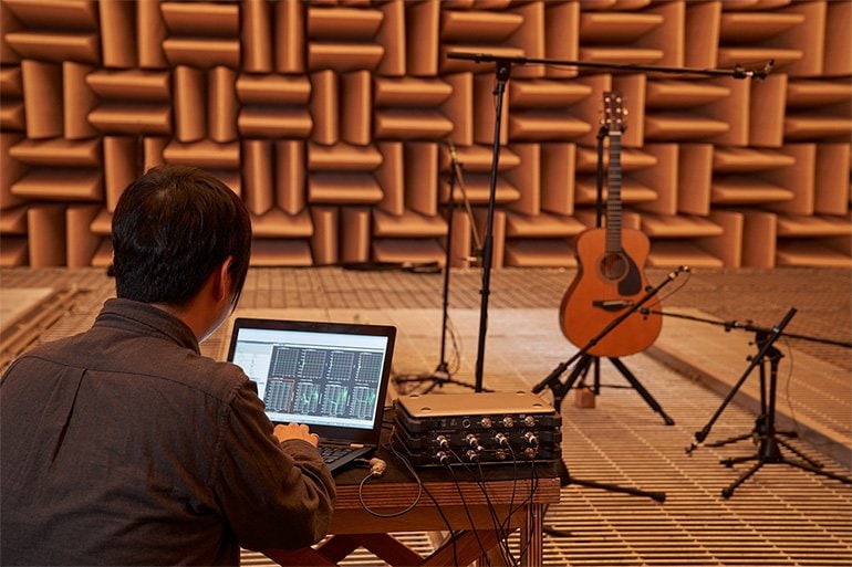 Engineer doing sound analysis on a laptop in an anechoic room with microphones pointed at FG guitar.
